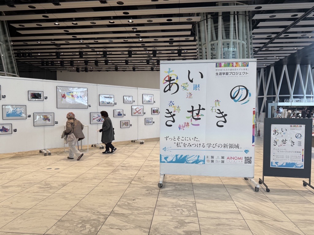せんだいメディアテーク オープンスクエアの「あいのきせき」展会場。あいのきせきのバナーと、壁に並んだ視線入力アート作品、来場者の様子